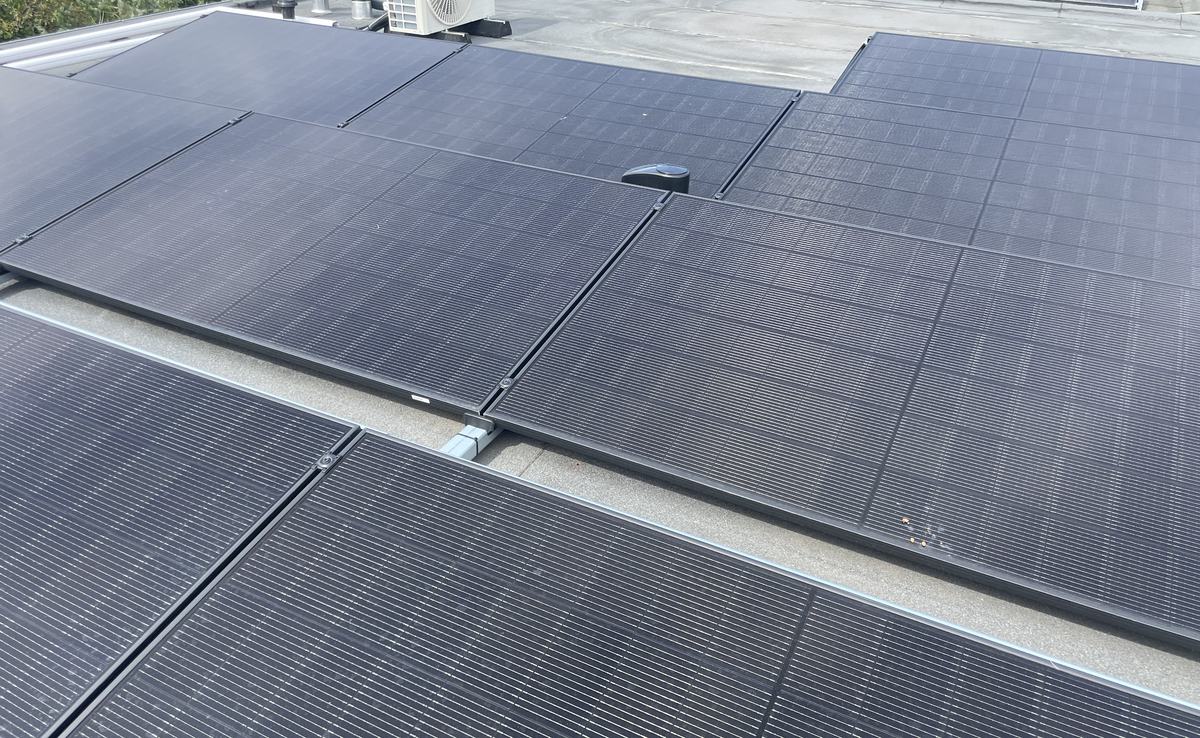 Zonnepanelen op een plat dak, met airco-units op de achtergrond
