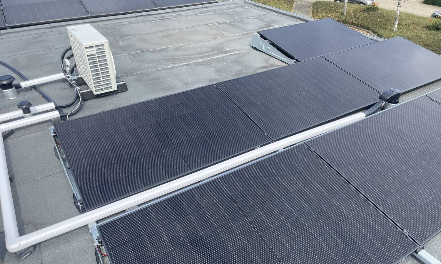 Plat dak vol zonnepanelen met daartussen de buitenunit van een airco